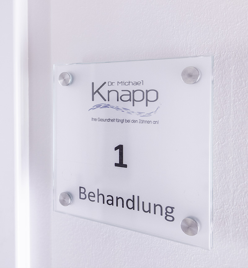 Ein Foto eines Behandlungszimmer-Schildes der Praxis Dr. Michael Knapp, auf dem eine "1" sowie der Zusatz "Behandlung" zu lesen sind